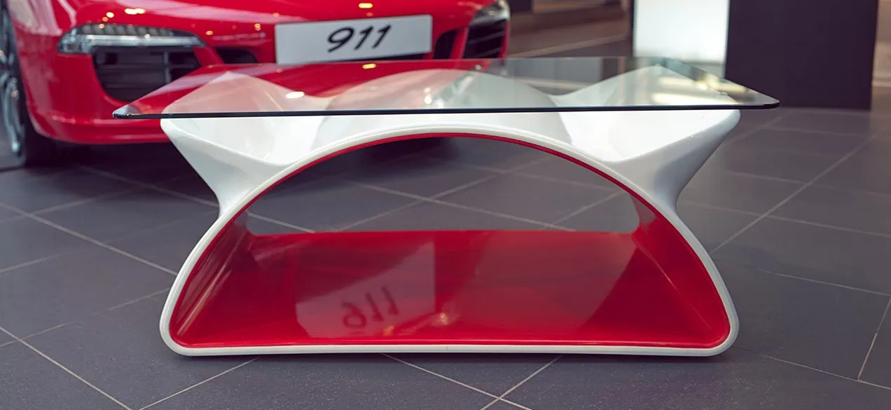 A white and red fibreglass table for a porsche showroom, shaped like an archway with two spoilers holding the glass surface.