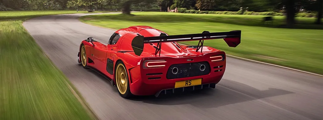 red ultima sports car driving at speed along a grass-lined road - with fibreglass body and spoiler manufactured by Quantum