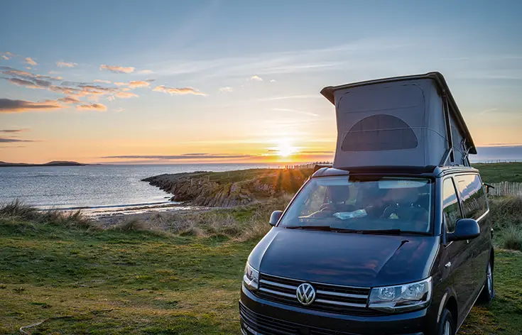 van with GRP pop-top roof parked by the beach at sunset