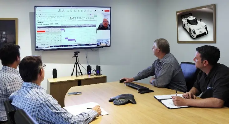 A manufacturing project management meeting with four people looking at a screen