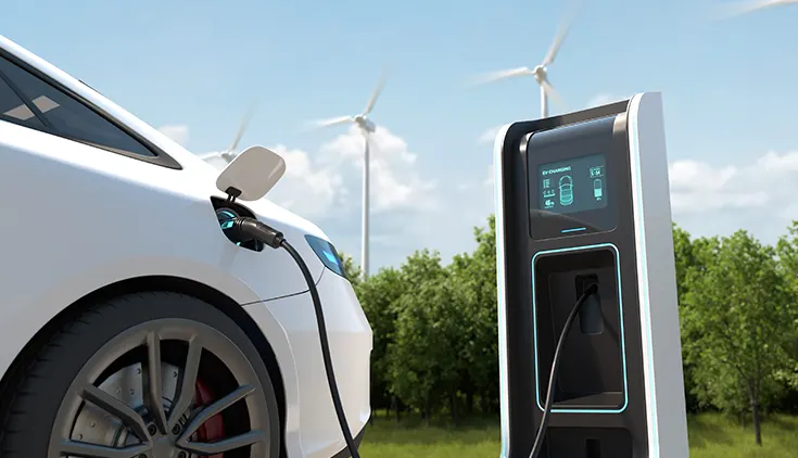 a car parked and charging at an EV charging station with a GRP shell. Wind turbines in the background.